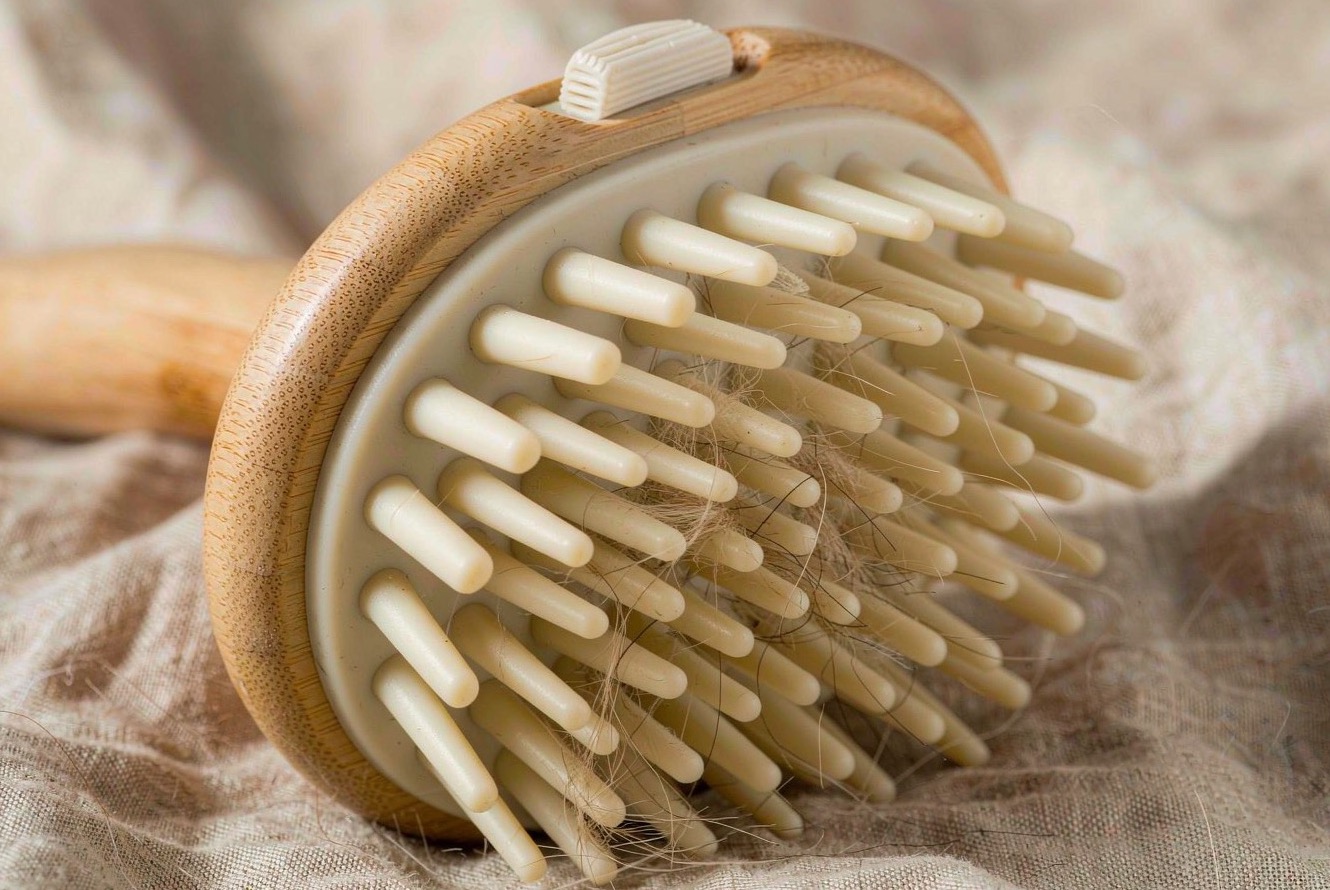 Close-up of a grooming brush showing the bamboo handle grain and flexible silicone bristle tips on a linen cloth.