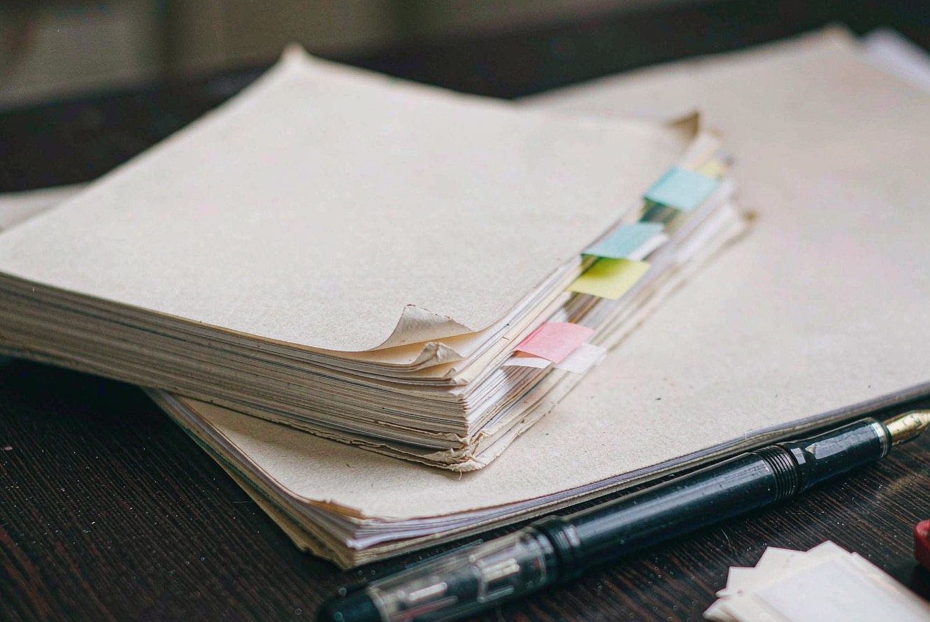 A stack of tabbed documents and a pen on a dark wooden desk.
