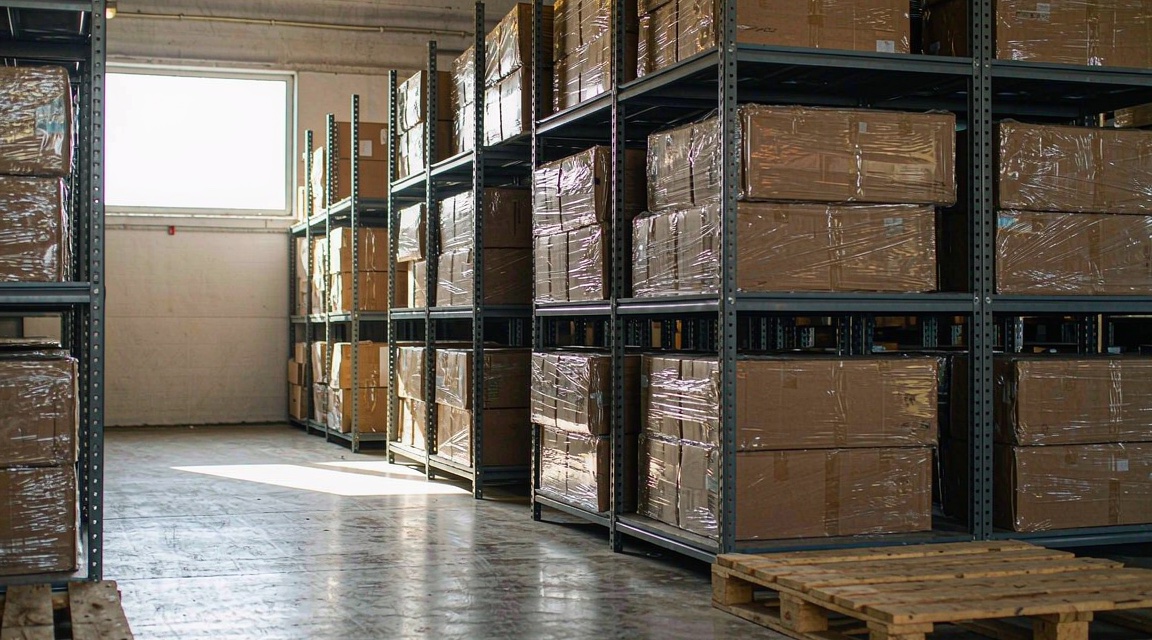 Warehouse shelving racks stacked with cartons and a wooden pallet in a tidy storage aisle
