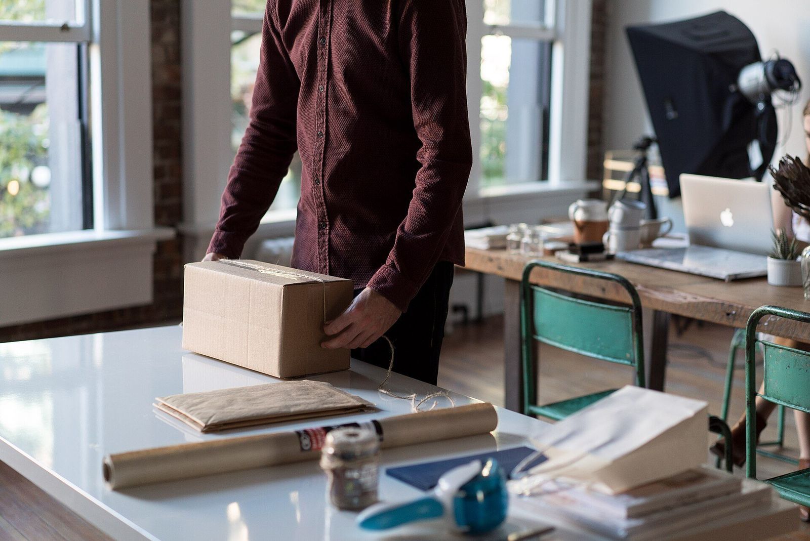 Hands folding protective paper around a plain cardboard carton on a work table