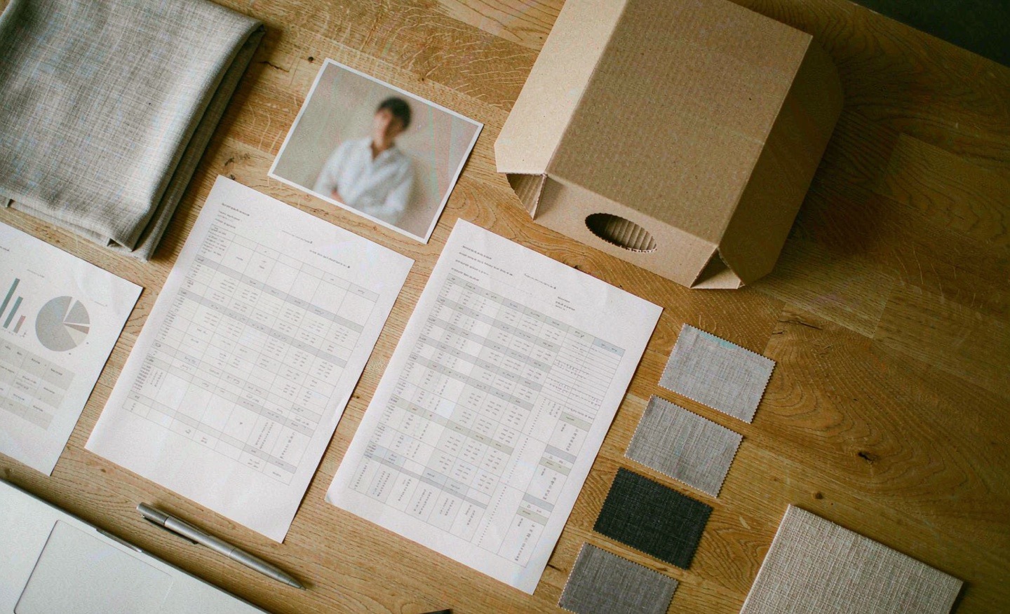 Overhead view of a desk with printed quotation sheets, material swatches and a packaging sample